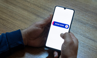 Close-up of the “Book Now” message on the smartphone screen. Online booking concept. Office background. Early booking message. 