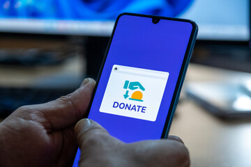Close-up of “Donate” message on smartphone screen. Online donation concept. Office background. Donate message. 