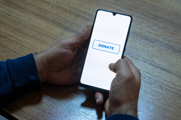 Close-up of “Donate” message on smartphone screen. Online donation concept. Office background....