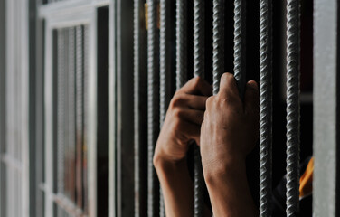 hands of a prisoner behind prison bars on black background	
