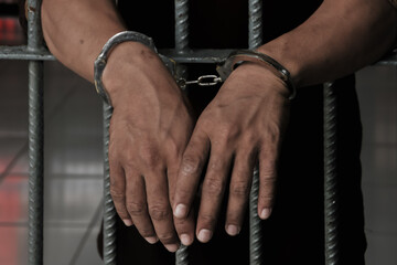 hands of a prisoner behind prison bars on black background	

