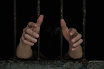hands of a prisoner behind prison bars on black background	
