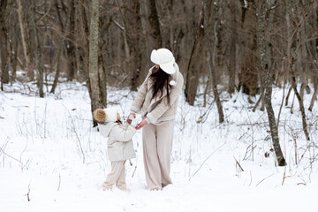 Happy active family mother and daughter in white fashion winter look have fun and walk in winter park, overjoyed mom and cute excited child girl spending weekend together outdoors in snowy frosty day