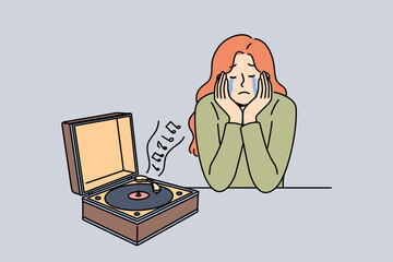 Woman cries listening to music on vinyl player, due to nostalgia and memories of happy past. Girl experiences nostalgia after launching retro device with audio album from last century