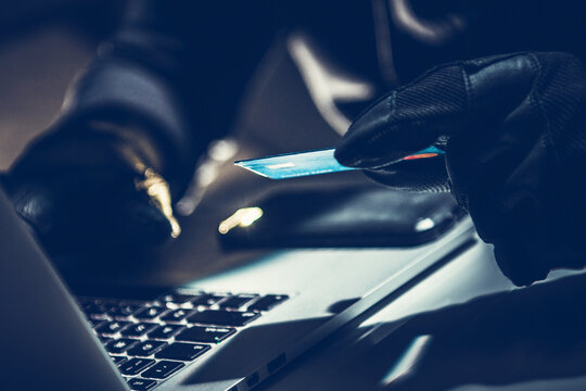 Criminal Using a Computer to Commit Fraud With a Credit Card at Night in a Dimly Lit Room