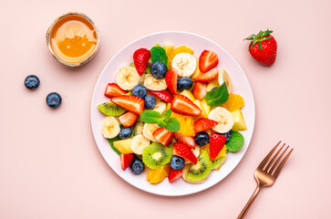 Yummy vegan fruit salad with strawberries, blueberries, banana, kiwi, orange and mint, pink background, top view