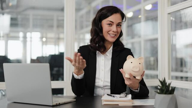 A businesswoman in a suit holds a piggy bank, smiles, and talks about savings and financial responsibility.