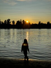 Fototapeta premium Child silhouette by lake at sunset