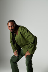 A stylish young man in a vibrant green ensemble poses confidently on a neutral grey background.