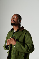 A young African American man showcases his fashion in a striking green outfit on a neutral backdrop.