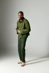 A stylish young man dressed in green attire strikes a confident pose on a grey background.