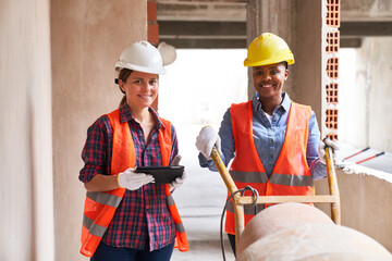 Portrait of smiling contractor with tablet PC standing by mason at incomplete corridor