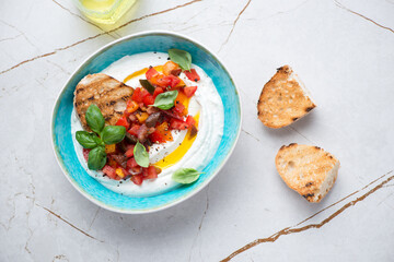 Turquoise bowl with ricotta dip, chopped tomatoes and ciabatta, above view on a white granite background, horizontal shot