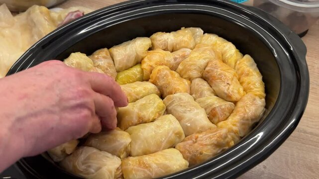 Traditional Serbian sarma being arranged in a slow cooker. These cabbage rolls are filled and wrapped, ready to be slow-cooked for a Slava celebration.