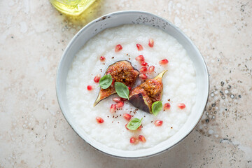 Bowl of rice porridge with fig fruits and pomegranate, horizontal shot on a beige granite background, elevated view