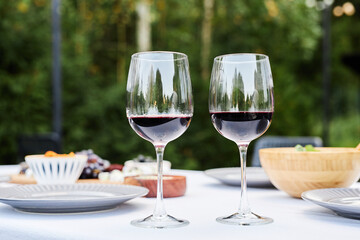 Closeup background image of two red wine glasses on festive dinner table outdoors set with crisp white cloth copy space