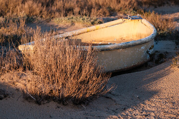 Old rowing boat in golden evening light on sandy walkway near bushes and dunes