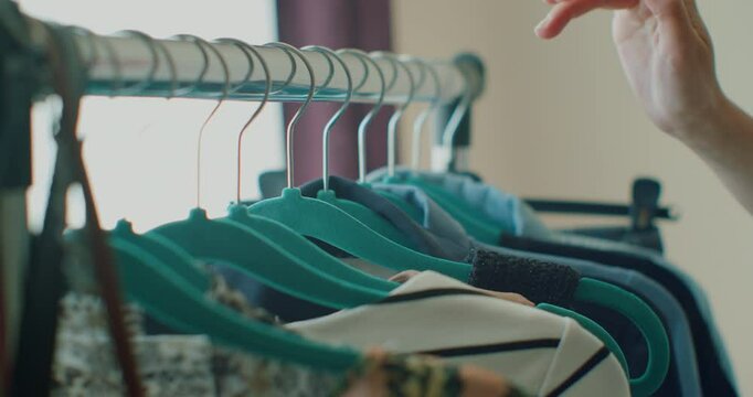 Close-up of female hands plucked a hanger with clothes. Woman's hands run across a rack of clothes. Woman's hand smoothing a colorful clothes. Close-up: a hanger for clothing.