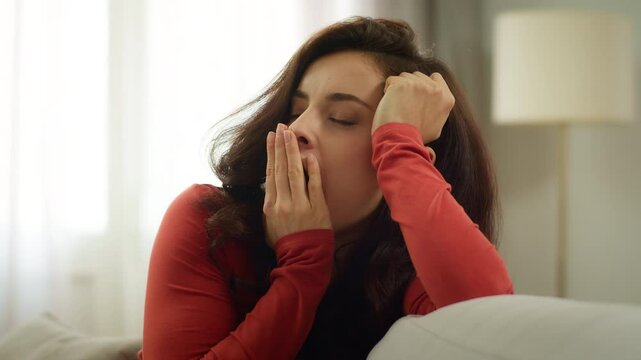Tired exhausted young Caucasian sleepy woman yawn bored female girl yawning hand over mouth homeowner stretching arms housewife stretch sitting couch sofa indoors living room. Boredom health problem