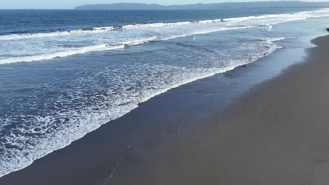 Waves and black sand at Kemiren Beach Cilacap with a background of blue sea and blue sky, 4K