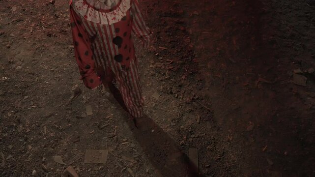 Crazy creepy killer man dressed as clown with makeup at attic in ruined house walks in stares at camera smile, top view. Halloween thriller concept.