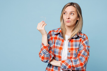 Young minded happy woman she wear red shirt t-shirt casual clothes hold in hands invisible aligners look aside on area isolated on plain pastel light blue background studio portrait Lifestyle concept