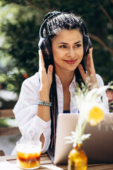 Woman with braided hair wearing headphones listening to music and sitting in a cafe and using laptop