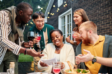 Vibrant shot of multiethnic group of adult friends looking at ultrasound image of Black young woman announcing pregnancy at party outdoors