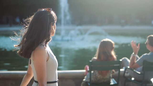 Portrait of a beautiful woman with sun glasses walking next to a fountain in a park, on bright summer day in paris