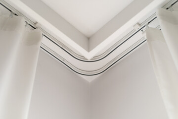 White curtains hanging from a metal track in a modern corner of a room during the daytime