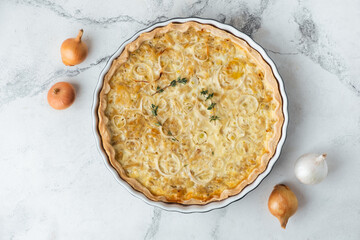 Flat lay of homemade onion cake on the white marble background. Quiche pie with steamed onions cheese and bacon
