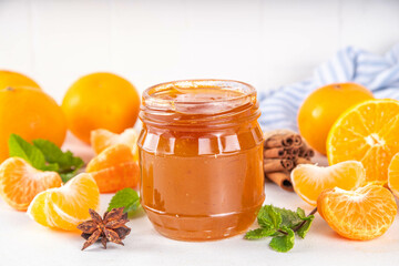 Golden sweet homemade tangerine jam, with spices and mint.  Sweet orange mandarin klementin jam or marmalade canning preserves in a jar, with whole and sliced tangerine on background