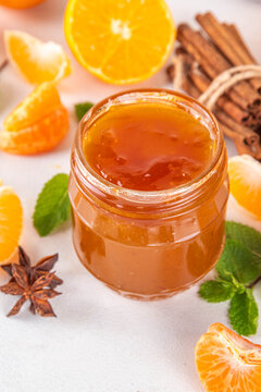 Golden sweet homemade tangerine jam, with spices and mint.  Sweet orange mandarin klementin jam or marmalade canning preserves in a jar, with whole and sliced tangerine on background