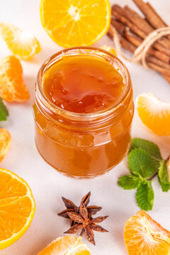 Golden sweet homemade tangerine jam, with spices and mint.  Sweet orange mandarin klementin jam or marmalade canning preserves in a jar, with whole and sliced tangerine on background