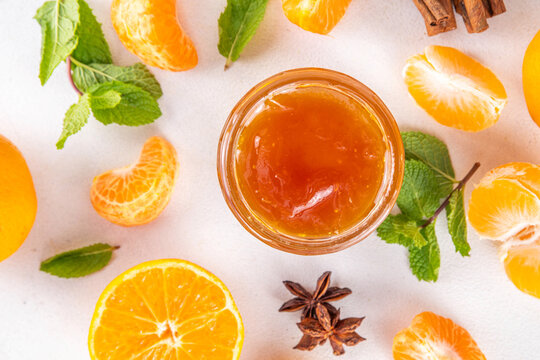 Golden sweet homemade tangerine jam, with spices and mint.  Sweet orange mandarin klementin jam or marmalade canning preserves in a jar, with whole and sliced tangerine on background