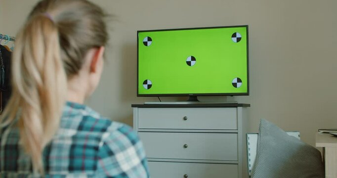 Television green screen, pretty girl watching modern TV at home and changing channels with remote control, movie and broadcasting. TV with horizontal green screen mock-up.