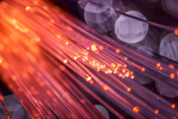 glowing fiber optic strands in vibrant orange and purple hues, creating a dynamic and energetic visual effect. The background features soft bokeh lights, enhancing the sense of depth and movement.