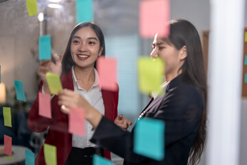 Two young businesswomen using sticky notes while brainstorming ideas