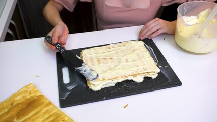 Making a cake. Hands spread cream on puff pastry layers.