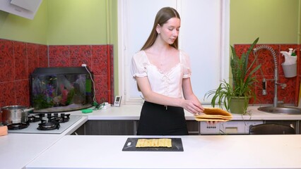 The girl is preparing food in the kitchen. She is shifting the cake layers.