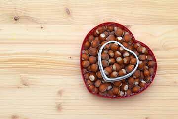 Obraz premium Hazelnuts in shell on heart shaped bowls, wooden background, copy space for text