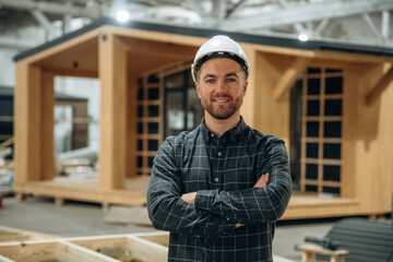 Cheerful facial expression. Male builder is at construction of wooden house
