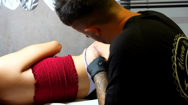 Tattoo artist creating delicate script tattoo on client's hips