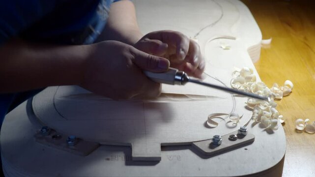 Luthier is using a chisel to carefully carve a piece of wood for a new violin in his workshop. He is working with precision and care to create a beautiful and resonant instrument