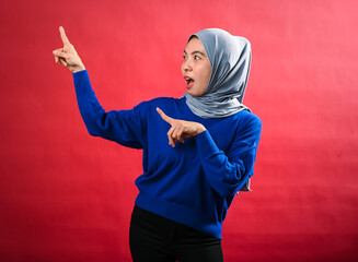 An Asian woman wearing a grey hijab and blue sweater points enthusiastically in two directions with...
