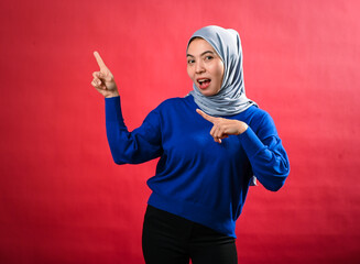An Asian woman wearing a grey hijab and blue sweater points enthusiastically in two directions with...