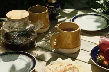 Tea party. Tea pot and ceramic mugs on wooden table outdoors.