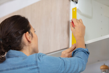 woman using spirit level and pencil marking shelf
