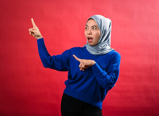 An Asian woman wearing a grey hijab and blue sweater points enthusiastically in two directions with...
