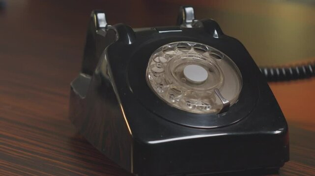Vintage black rotary telephone resting on a polished wooden desk. The nostalgic design evokes a sense of retro communication and timeless aesthetics in a classic setup.